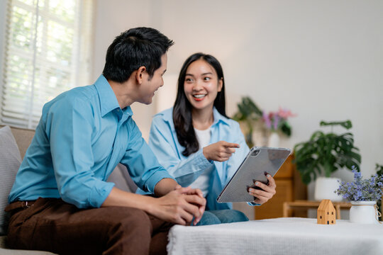 Young asian couple browsing tablet, reviewing home design plans together in living room setting - Powered by Adobe