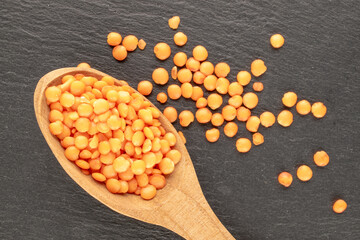 Red lentils with a wooden spoon on a slate stone, close-up, top view.