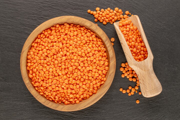 Red lentils on a wooden plate on a slate stone, close-up, top view.