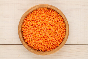 Red lentils on a wooden plate on a wooden table, close-up, top view.