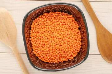 Red lentils in a ceramic plate with a wooden spoon on a wooden table, close-up, top view.