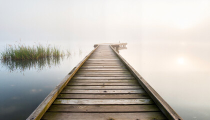 Naklejka premium Misty wooden dock outstretching into serene lake, peaceful solitude