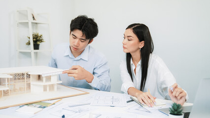 Professional male engineer measure house model by using ruler while beautiful cooperative coworker...