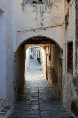 Narrow alley with tunnel and with whitewashed walls and stone pavement leading to a courtyard in the Greek Islands, Greece