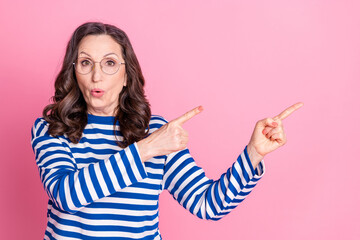 Portrait of a cheerful senior woman in a striped shirt pointing playfully against a colorful pink...