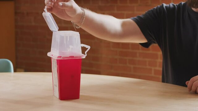 Man performs the proper disposal procedure of a used needle into a sharps container, emphasizing safety and hygiene in a healthcare setting.