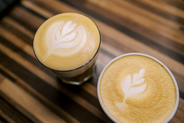 Two cups of cappuccino with leaves on the foam stand on a wooden table