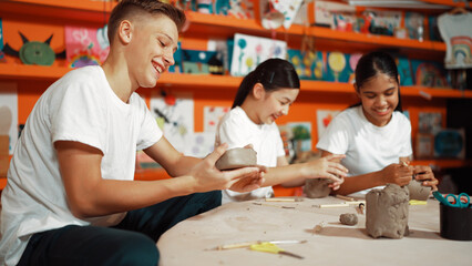 Caucasian smart teenager modeling clay while craving glass of clay at art lesson. Group of...