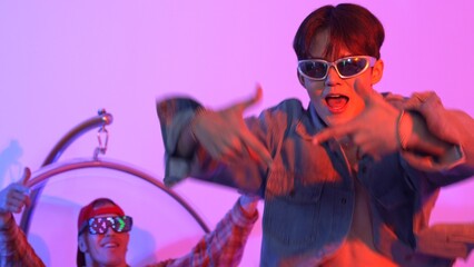 Close up of asian street dancer moving to pop music with neon light while diverse friend sitting and support performance. Professional performer practicing dancing step to beat at studio. Regalement.