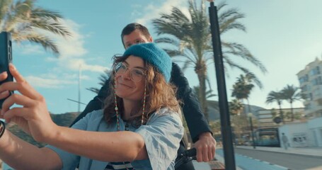 Cute modern couple on date ride on cargo bicycle at beach boardwalk. Girlfriend make content on mobile phone, film selfie of her boyfriend. Sit in front of cargo electric bicycle on sunny warm day