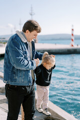 Smiling dad leads little girl by the hands along a rope fence on the seashore