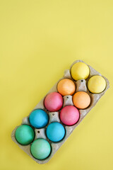 Colorful Easter eggs in a carton on a yellow background