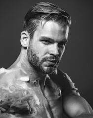 Obraz premium Closeup portrait of handsome man washing body with sponge and moisturizing gel. Men's body care cosmetic. Serious guy taking shower in bathroom. Skincare, hygiene and morning routine. Black and white.