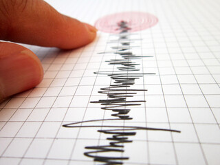 Seismograph and earthquake. A hand pointing at a seismograph recording the seismic activity of an...
