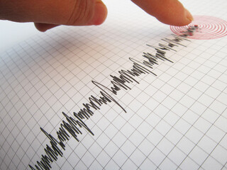 Seismograph and earthquake. A hand pointing at a seismograph recording the seismic activity of an...