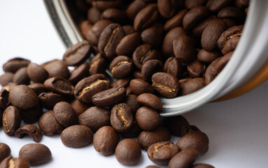 Close up of coffee beans spilling out of a coffee jar. Roasted coffee beans on white background