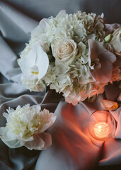 Elegant flower arrangement with white roses and orchids on a silky cloth with a glowing candle