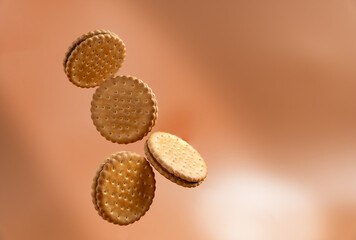 Four cookies are flying in the air on a brown background. They are all the same size and shape. They are brown and have chocolate filling.