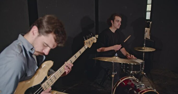 A jazz trio practices in a dark room. The bass player and drummer are focused and work together, jamming before a concert.