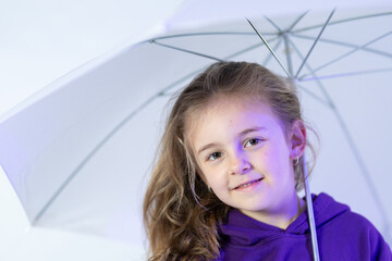 Smiling young girl in purple hoodie holding an umbrella on a white background
