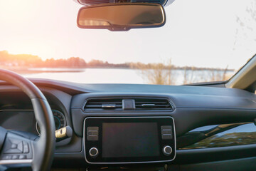 Car interior with a modern dashboard and rear-view window with serene lake with trees lining the shore, under a clear sky ckground