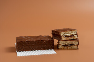 A chocolate cake lies on white paper. Another cake is cut in half. Both cakes are on a brown background.