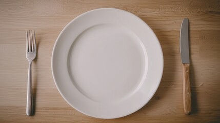 A simple dining setup featuring a plain white plate, a fork, and a knife on a wooden table.