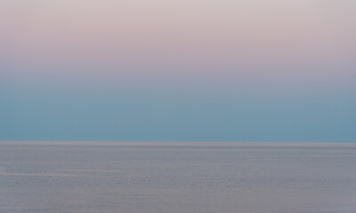 Calm sea reflecting pastel colors of sunrise sky
