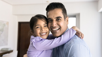 Fototapeta premium Close up portrait of happy Indian father and small 5s adorable daughter cuddling, laughing, looking at camera with joyful expression, exuding unconditional love and support and tenderness. Family ties