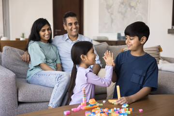 Parents sit on sofa, two children play together, give high five, start or finish game with colorful...