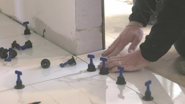 Construction worker placing tile leveling system spacers on floor