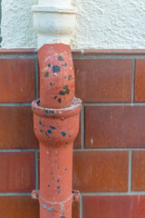 Rusty water pipe with chipped paint against tiled wall in urban setting under evening light