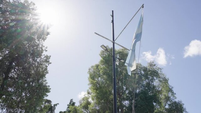 Bandera argentina flameando en m&aacute;stil bajo el sol brillante, cielo despejado y viento suave