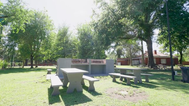 &Aacute;rea de asado y camping en d&iacute;a soleado: parrilla, fuego, mesas de picnic, entorno natural, ambiente relajado y soleado
