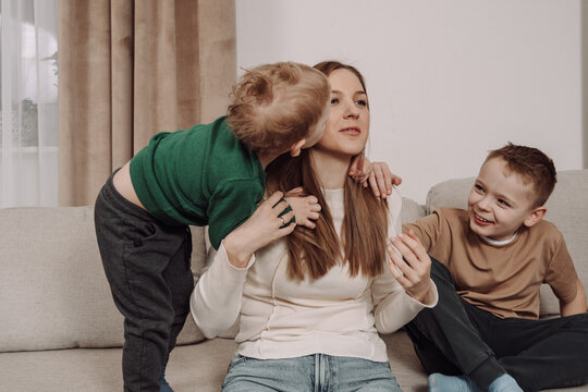 A happy mother embraces her children in a warm, homey atmosphere. The younger boy kisses her cheek, while the older one smiles joyfully. A natural, heartfelt family moment full of love and closeness.
