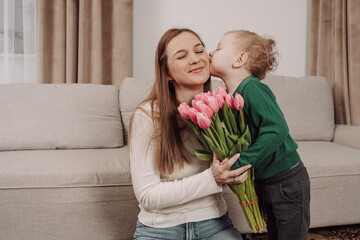 A young boy gives his mother a beautiful bouquet of pink tulips, bringing joy and warmth to the moment. A heartfelt gesture symbolizing love, appreciation, perfect for Mother's Day and Women's Day.