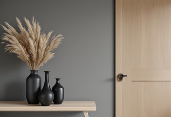 Pampas grass and black vases on a wooden table against a grey wall.