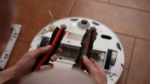 View from shoulder of unrecognizable person comparing new brush with worn one from robot vacuum cleaner during maintenance procedure. Concept of importance of regular upkeep. Shooting in slow motion.