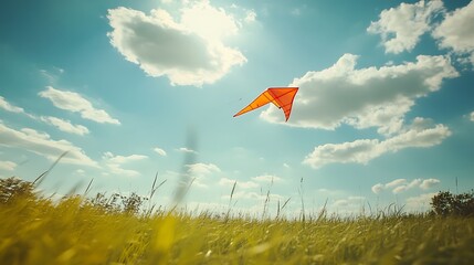 Orange kite flying high in a vibrant blue sky above a green field.