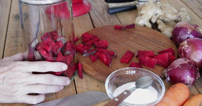 Red beet root naturally fermented kvass preparing, filling glass jar with beetroot slices, closeup