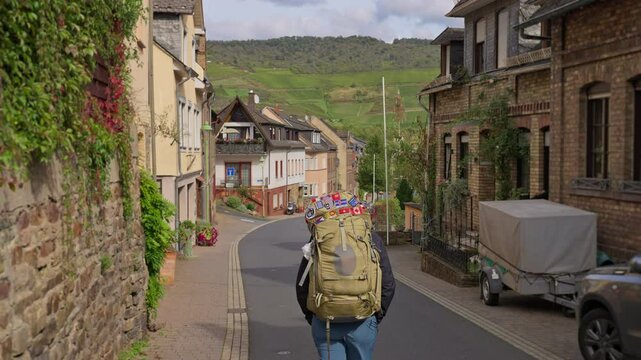 Trekking hiker walking through a small Rhine Valley town surrounded by hillside vineyards on a sunny autumn day, Germany