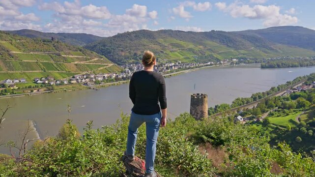 Moving towards rear view of hiker standing and enjoys valley view from hilly viewpoint over the Rhine River Valley, Germany