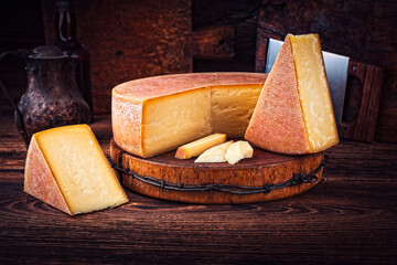Traditional artisan handcrafted rustic hard mountain cheese wheel on an old wooden board in a...