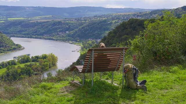 Backpacker relaxing on bench at a viewpoint overlooking the Rhine River Valley on a sunny summer day, Germany