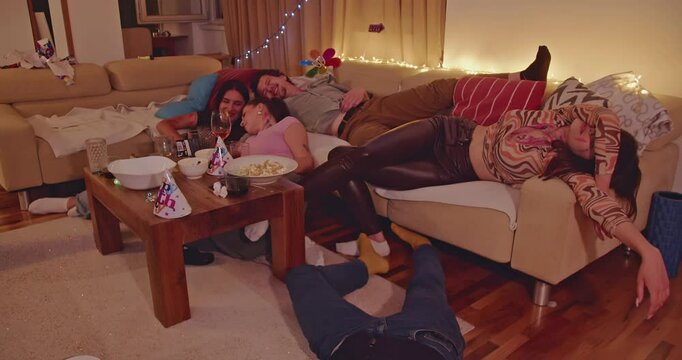 Friends sleeping after a crazy house party. Empty plates and glasses on the table. The room is a mess after the celebration.