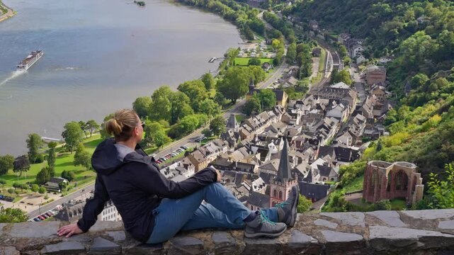 A young woman admires the picturesque view over the medieval old town of Bacharch with tracking movement, Rhine Valley, Germany