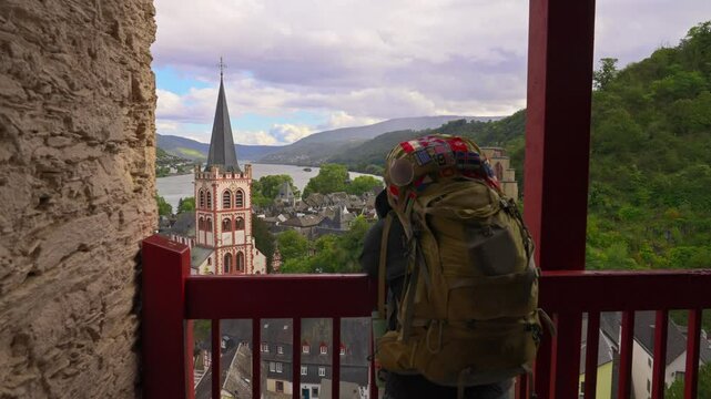Moving past hiker with backpack to reveal the picturesque Rhine River Valley town of Bacharach during the summer, Germany