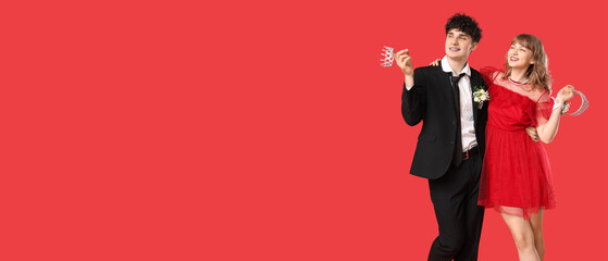 Happy prom couple holding crowns on red background