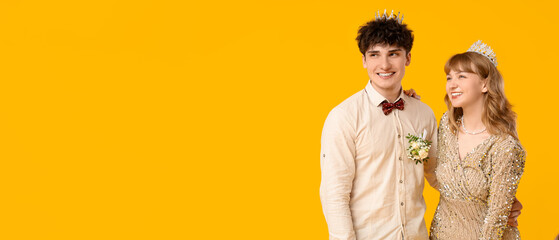 Happy prom couple in crowns on yellow background