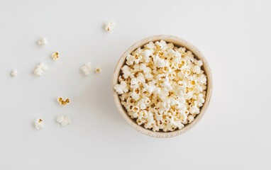 Overhead shot of a bowl of popcorn on a white background.  A few popcorn pieces are scattered around the bowl. The bowl is speckled beige